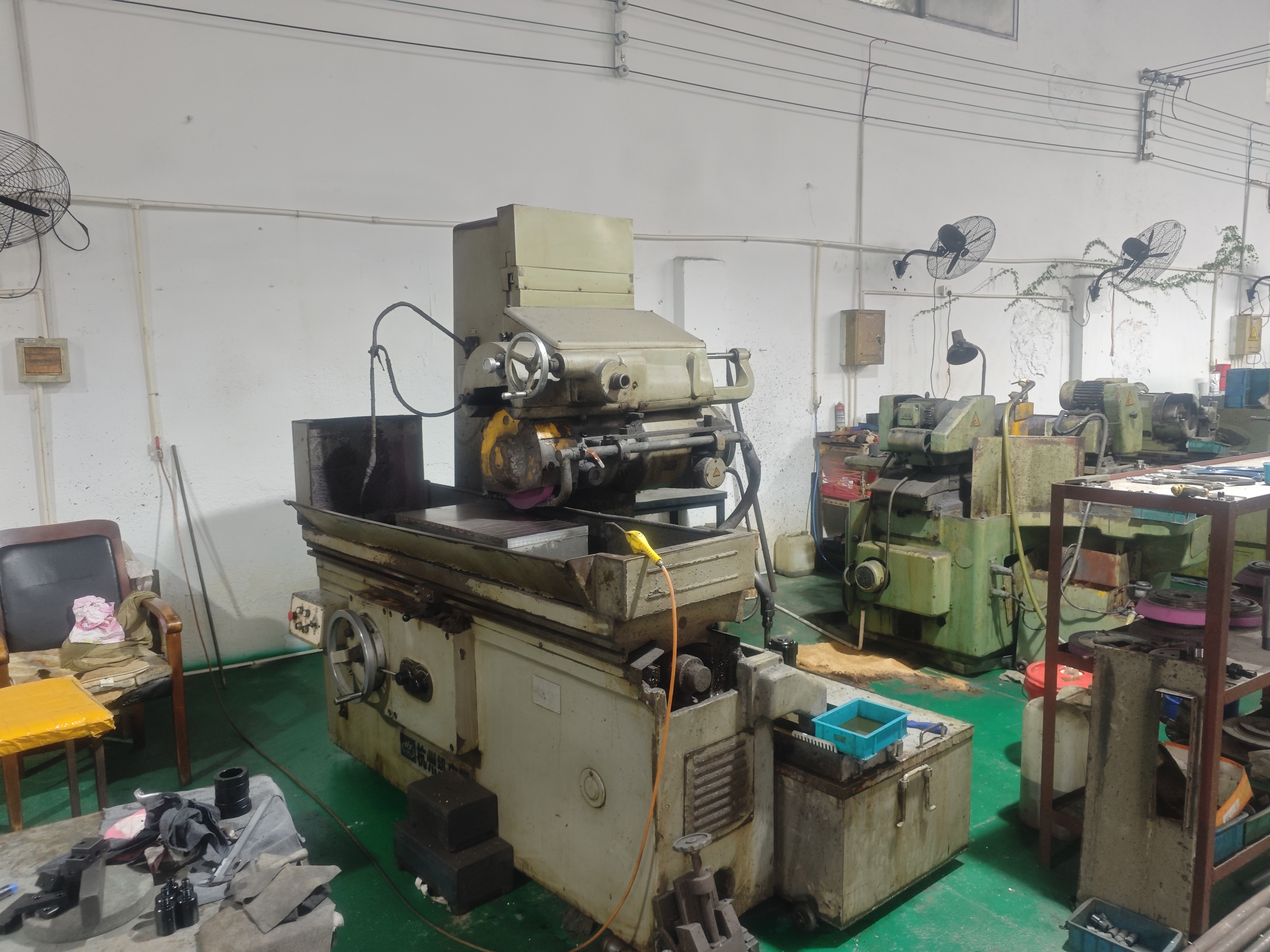 Surface grinding machine with further grinders in the background of the workshop